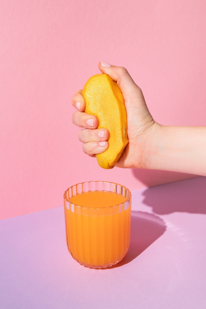 Hand squeezing a lemon over a glass of tropical bia BLENDS on a pink and purple gradient background