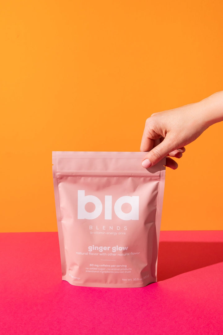 bia BLENDS healthy ginger energy drink being held against an orange and pink background